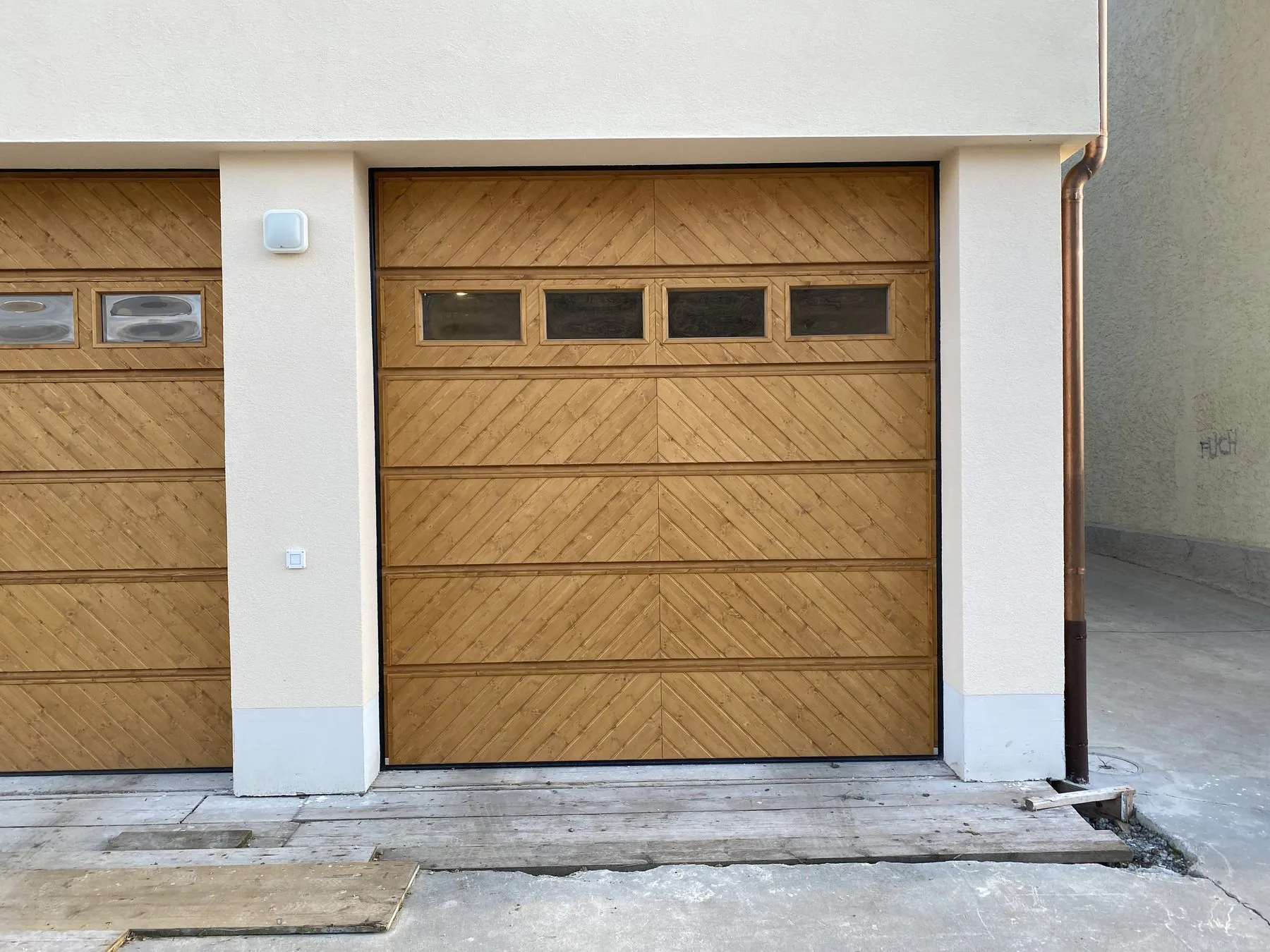 Echtholz-Sektionaltor mit diagonaler Fischgrät-Schalung und Fensterreihe an einem hell verputzten Neubau