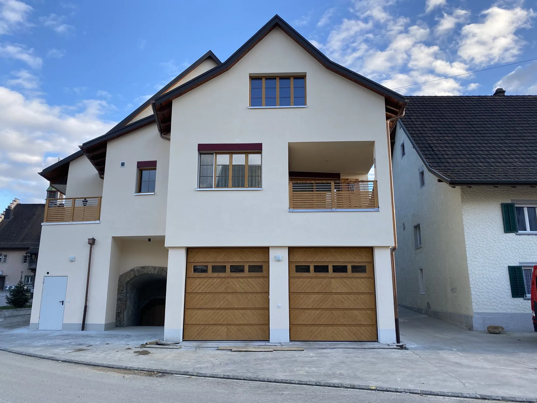 Zwei Sektionaltore aus Echtholz mit Fensterreihe an einem neuen Mehrfamilienhaus neben einem älteren Wohnhaus