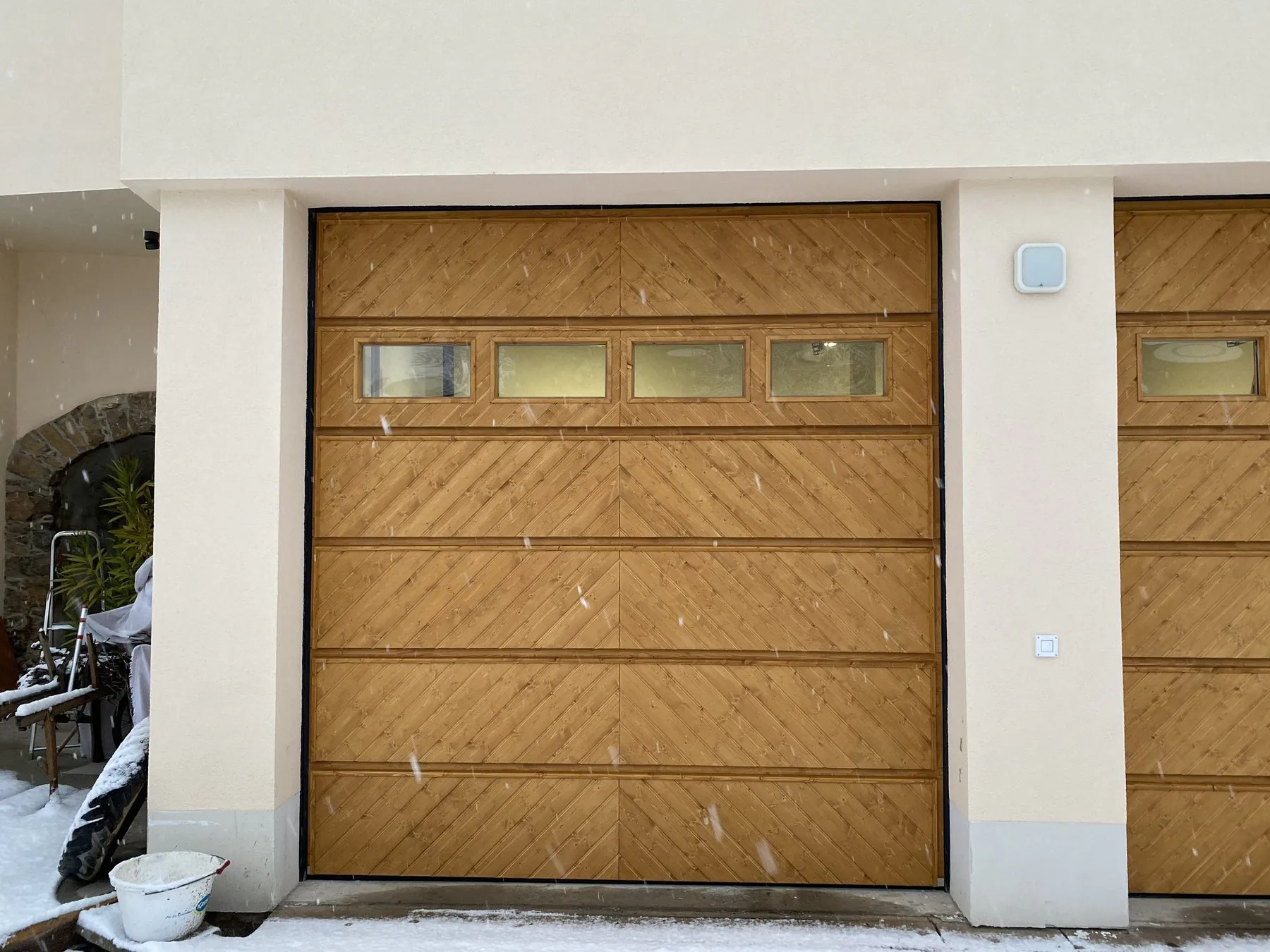 Garagentor aus Holz mit diagonaler Fischgrät-Schalung und Fensterreihe an einer hellen Fassade, daneben ein zweites Tor