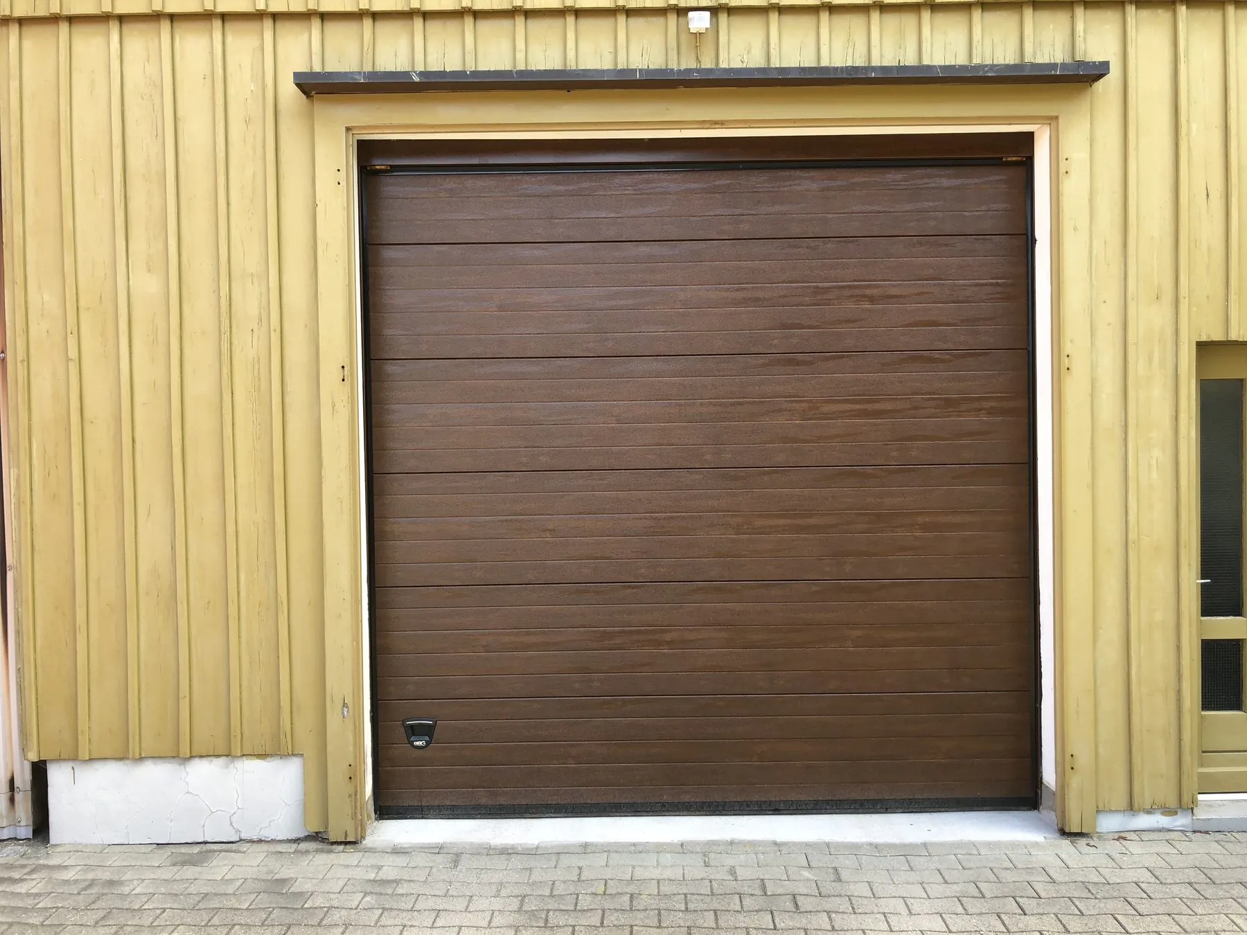 Braunes Sektionaltor in Holzoptik mit Bodendichtung in einer gelb gestrichenen Holzfassade