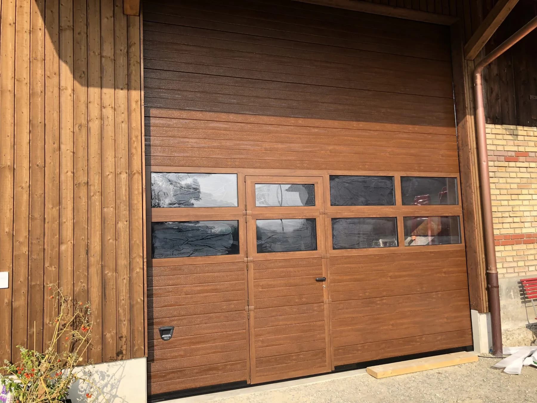 Hohes Sektionaltor in Holzoptik mit Schlupftür und Fensterband in einer umgebauten Scheune