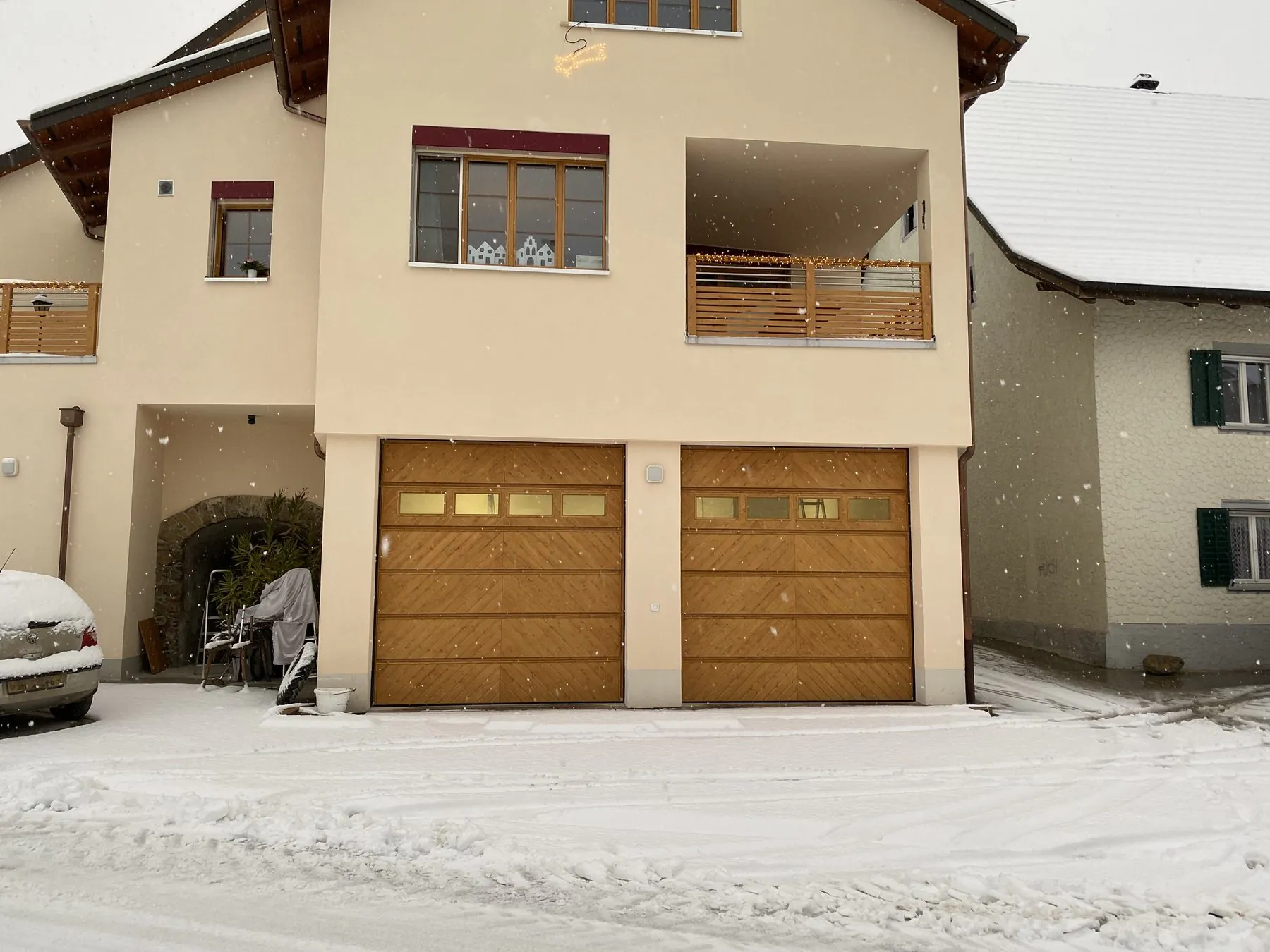 Zwei Holz-Garagentore mit Fensterreihe an einem Wohnhaus bei Schneefall