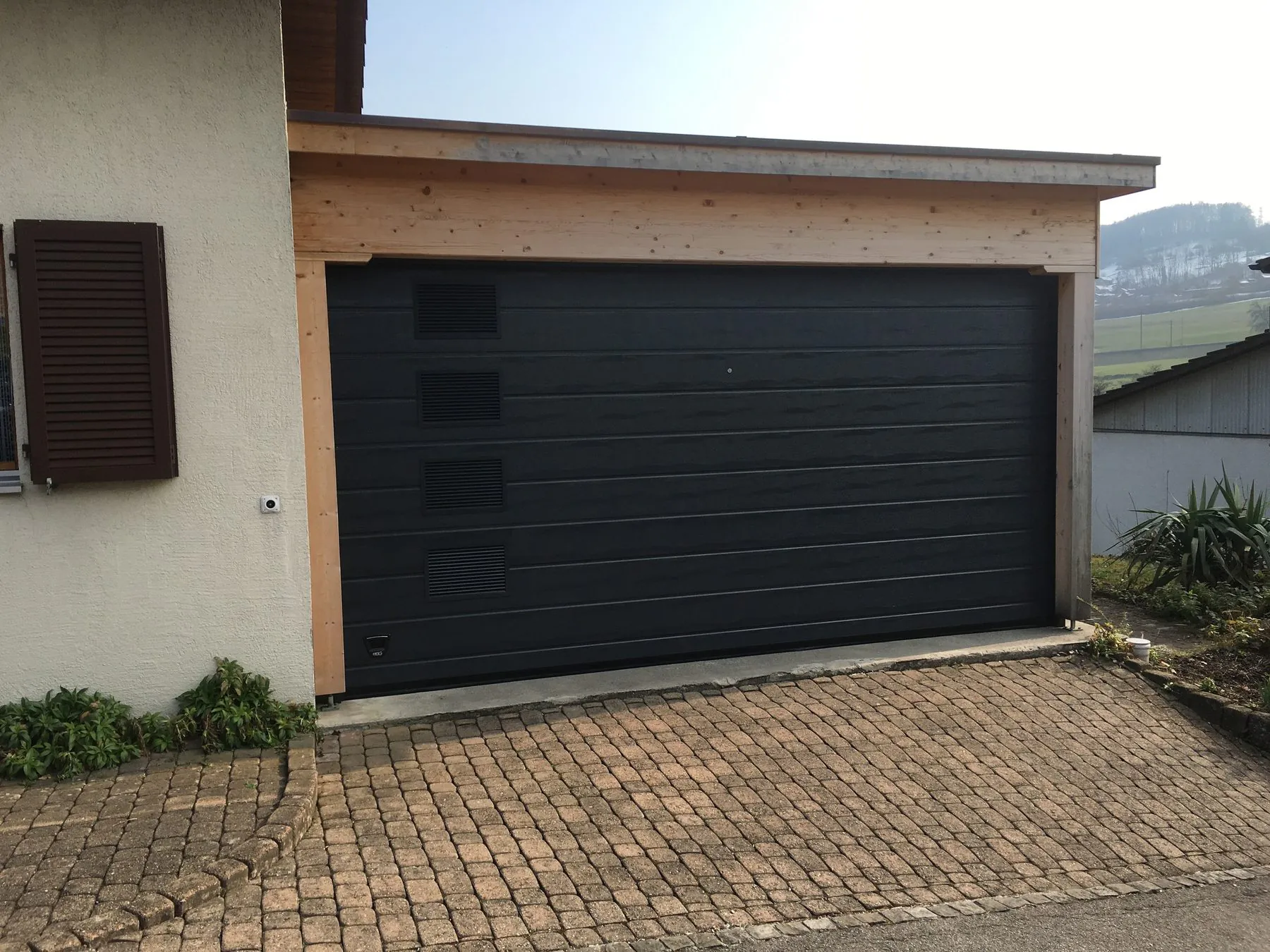 Anthrazitfarbenes Sektionaltor neben einem Carport