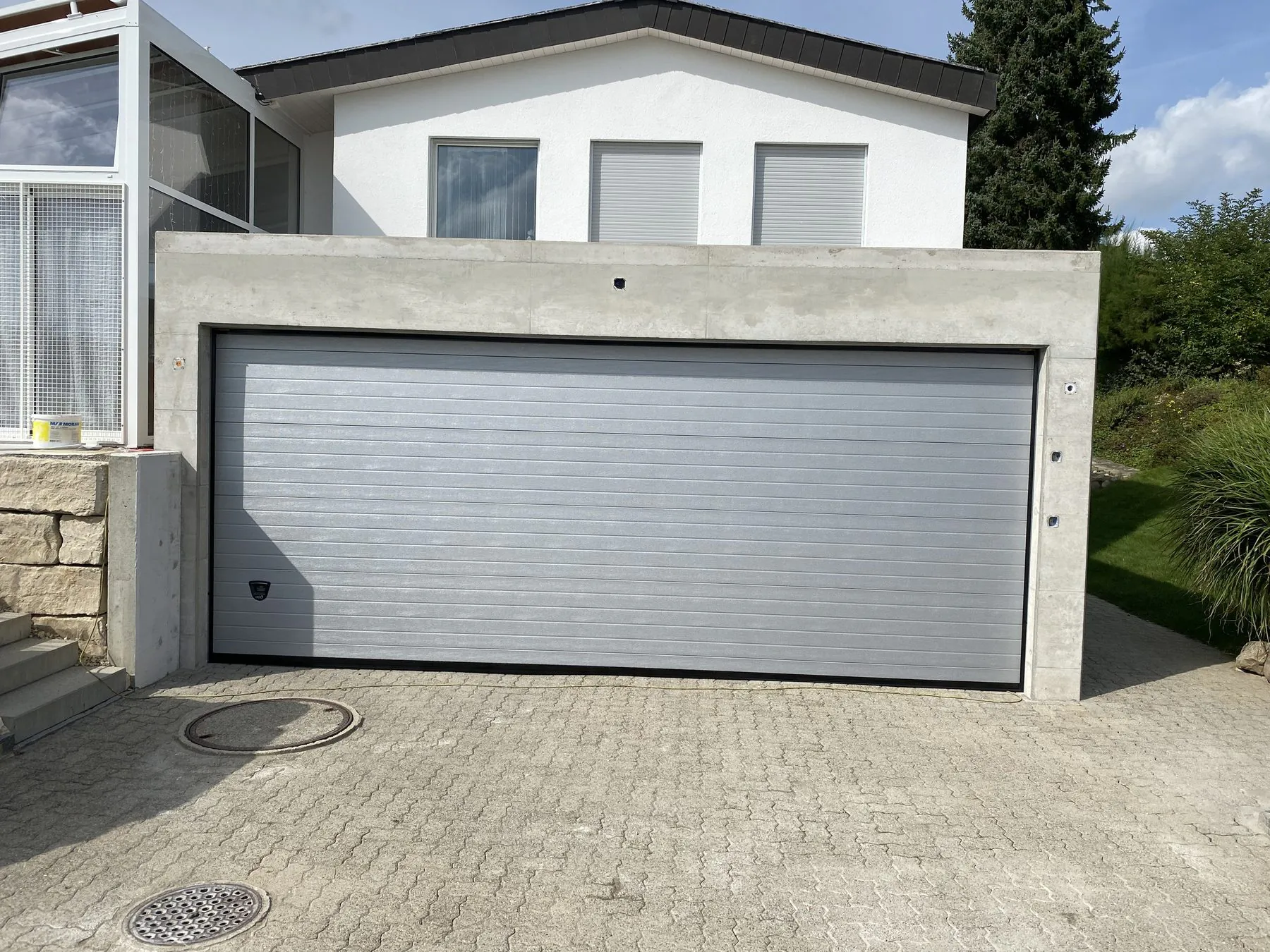 Hellgraues Sektionaltor an einer Garage mit gepflasterter Einfahrt