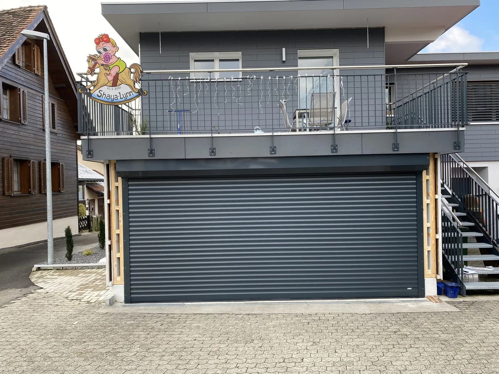 Anthrazitfarbenes Rolltor an einem Mehrfamilienhaus mit Holzverkleidung